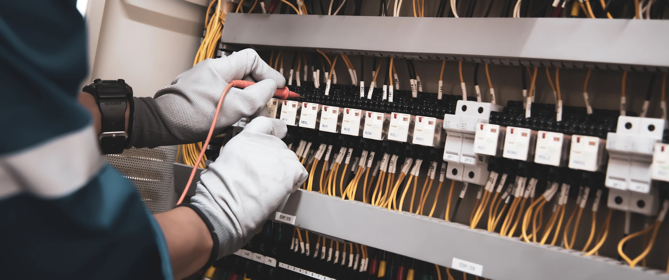 Électricien professionnel en tenue de travail et équipement de sécurité (casque, gants isolants) effectuant une intervention électrique en intérieur, travaillant sur une installation ou un tableau électrique. La scène doit montrer l'électricien concentré sur son travail, avec ses outils visibles, dans un environnement résidentiel ou professionnel réaliste, capturant la compétence et la disponibilité professionnelle de l'électricien.